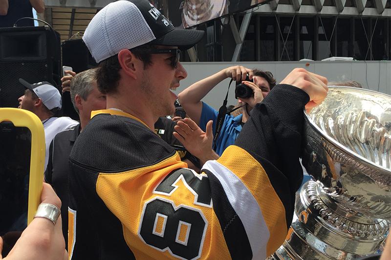 Sidney Crosby carries the Stanley Cup through a crowd of fan as he exits the stage.