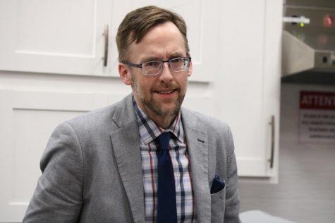 Picture of Jonathan Potts. In a heather gray suit, with a plaid shirt, and navy blue tie.